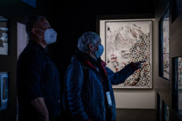 Martha Cooper und Jaime Rojo betrachten Video- und Fotoarbeiten in einem abgedunkelten Ausstellungsraum der Martha-Cooper-Ausstellung im Urban Nation Museum.