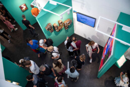 Blick von oben in die Ausstellung mit grünen Stellwänden, Besuchern und einer „1UP“-Skulptur im URBAN NATION Museum.