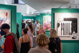 Ausstellungsraum mit Besuchern und großformatigem Werk „PRIVILEGE“ auf grünen Stellwänden im URBAN NATION Museum.