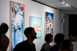 Besucher vor mehreren Gemälden in einem Ausstellungsbereich des URBAN NATION Museums, „Talking and other Banana Skins“.