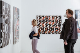 Zwei Besucher betrachten Details einer großformatigen Layer-Cake-Arbeit aus THE VERSUS PROJECT bei URBAN NATION.