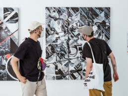 Zwei Besucher betrachten ein großformatiges Werk aus THE VERSUS PROJECT von Layer Cake in der URBAN NATION Ausstellung.