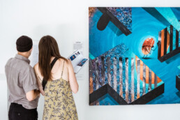 Zwei Besucher vor einem türkisfarbenen Werk aus THE VERSUS PROJECT von Layer Cake in der URBAN NATION Ausstellung.