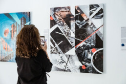 Besucherin fotografiert ein Werk aus THE VERSUS PROJECT von Layer Cake in der URBAN NATION Ausstellung.