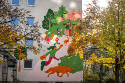 Vikunia Fassadenbild in der Mudrastraße für bbd mit Parkszene, Figuren und Hund zwischen Bäumen im Herbstlicht.