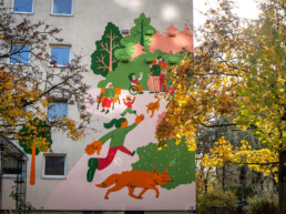 Vikunia Fassadenbild in der Mudrastraße für bbd mit Parkszene, Figuren und Hund zwischen Bäumen im Herbstlicht.