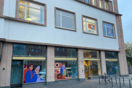 Fassadenansicht des Dokumentationszentrums mit mehreren Fensterillustrationen von Vikunia im Erdgeschoss und Obergeschoss.