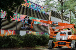 Künstler bei der Umsetzung der ONE WALL von Lukas Zeilinger am Parkhaus in Berlin Staaken mit großer Hebebühne im Vordergrund